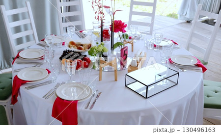 White draped round table featuring floral centerpiece, scattered fruits, numbered five, set for elegant outdoor dining event with sophisticated reception styling White draped round table featuring floral centerpiece, scattered fruits, numbered five, set for elegant outdoor dining event with sophisticated reception styling 130496163