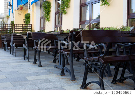 Peaceful outdoor cafe scene with benches and tables under the shade, creating perfect space for relaxation. Neat arrangement and surrounding greenery invite guests to enjoy urban dining Peaceful outdoor cafe scene with benches and tables under the shade, creating perfect space for relaxation. Neat arrangement and surrounding greenery invite guests to enjoy urban dining 130496663