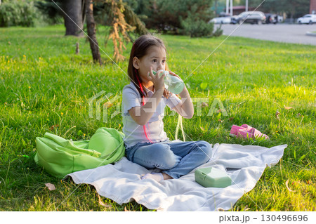 Young girl enjoying a refreshing drink on a picnic blanket in a park setting Young girl enjoying a refreshing drink on a picnic blanket in a park setting 130496696