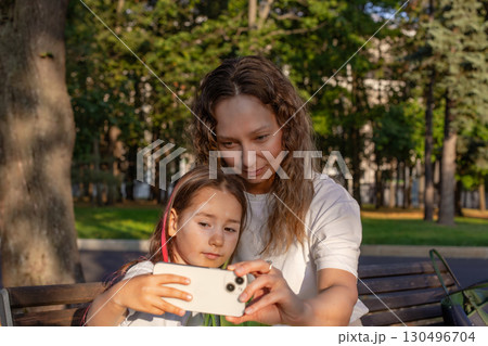 Mother and daughter taking selfie on park bench during sunny day Mother and daughter taking selfie on park bench during sunny day 130496704