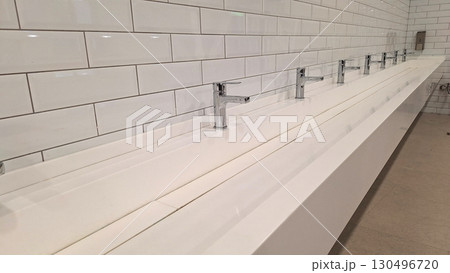 Modern public restroom with white tiled walls and chrome faucets Modern public restroom with white tiled walls and chrome faucets 130496720