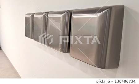 Row of stainless steel hand dryers on white tiled wall in public restroom Row of stainless steel hand dryers on white tiled wall in public restroom 130496734