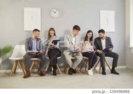 Smiling business people sitting in row with clipboards, preparing for interview or business meeting. Smiling business people sitting in row with clipboards, preparing for interview or business meeting. 130496966