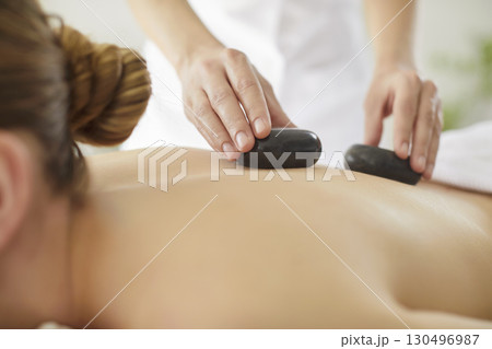 Therapist, cosmetologist applying stones to female back, woman client treatment, hot stone therapy Therapist, cosmetologist applying stones to female back, woman client treatment, hot stone therapy 130496987