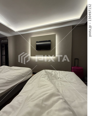 Hotel room interior with beds and illuminated wall-mounted television. Hospitality, travel, and lifestyle representing rest, comfort, and modern lodging atmosphere. Hotel room interior with beds and illuminated wall-mounted television. Hospitality, travel, and lifestyle representing rest, comfort, and modern lodging atmosphere. 130497132