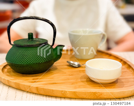 Green cast iron teapot with cup and spoon on wooden tray. Beverage, hospitality, and lifestyle highlighting tradition, refreshment, and cultural dining ritual. Green cast iron teapot with cup and spoon on wooden tray. Beverage, hospitality, and lifestyle highlighting tradition, refreshment, and cultural dining ritual. 130497184
