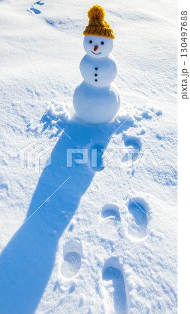 ニット帽をかぶった雪だるまと足跡のある雪景色 ／ 冬の可愛らしさと温かみを伝えるイメージ素材 130497688