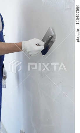 Professional construction worker wearing blue work overall is using a finishing trowel to carefully apply plaster on a wall, demonstrating expertise in home renovation 130497696