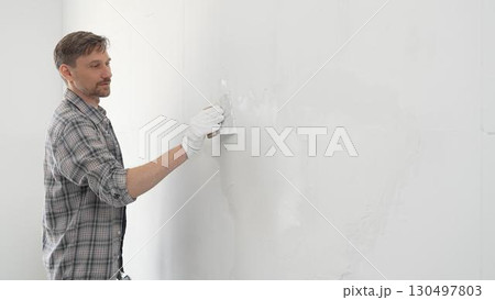 Construction worker spreading plaster on white wall, wearing protective gloves and t-shirt during home renovation project, working with professional skill and focus 130497803
