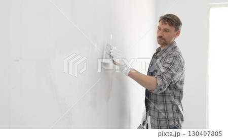 Construction worker spreading plaster on white wall, wearing protective gloves and t-shirt during home renovation project, working with professional skill and focus Construction worker spreading plaster on white wall, wearing protective gloves and t-shirt during home renovation project, working with professional skill and focus 130497805