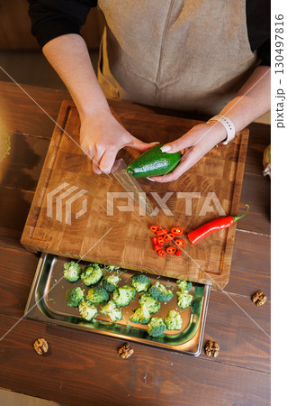 Woman slicing fresh avocado on wooden cutting board in cozy rustic kitchen Woman slicing fresh avocado on wooden cutting board in cozy rustic kitchen 130497816