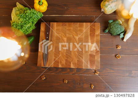 Top view of cutting board with knife surrounded by fresh vegetables on a rustic wooden table 130497828