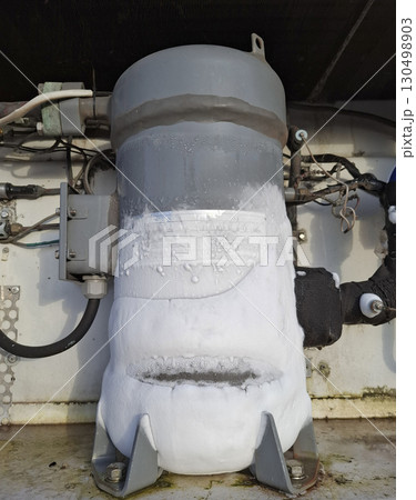 A heavy-duty refrigerator motor covered in frost is seen in an industrial setting, indicating low operational temperatures. 130498903