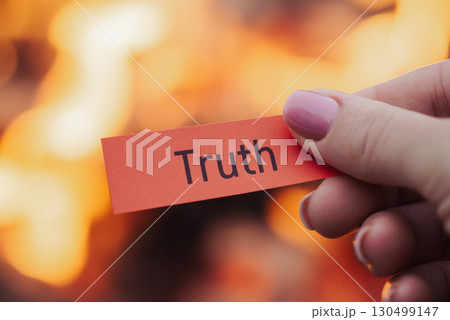 Paper with inscription Truth in woman's hand with fire on the background. Hiding truth from someone`s concept, lie and false Paper with inscription Truth in woman's hand with fire on the background. Hiding truth from someone`s concept, lie and false 130499147