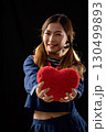 Smiling young woman in blue outfit school uniform holding fluffy red heart forward against dark background 130499893