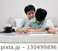 A father guides his young son in drawing with colored pencils at a table, sharing a creative bonding moment together at home 130499896
