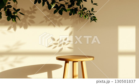 A simple wooden table with a round top filled with a coating that provides sunlight. The delicate shadows of leafy branches play on the textured cream wall in the background. 130501837