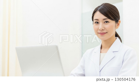 ノートパソコンの前で白衣を着た若い女性 130504176