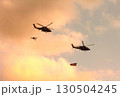 日米の国旗を吊るして紅に染まる夕空を編隊飛行する米海軍のMH-60Rシーホーク艦載ヘリコプター 130504245