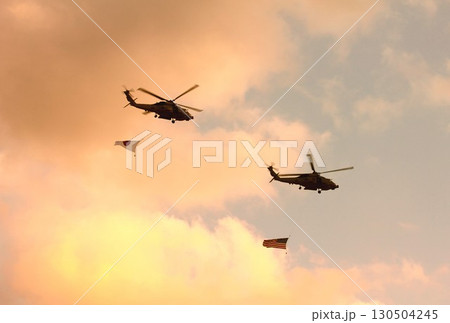 日米の国旗を吊るして紅に染まる夕空を編隊飛行する米海軍のMH-60Rシーホーク艦載ヘリコプター 130504245