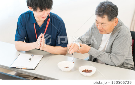 介護施設,病院,リハビリセンターで豆つかみトレーニンングをする男性患者と介護士の男性 130506729
