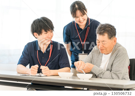 介護施設,病院,リハビリセンターで豆つかみトレーニンングをする男性患者と介護士の男女スタッフ 130506732