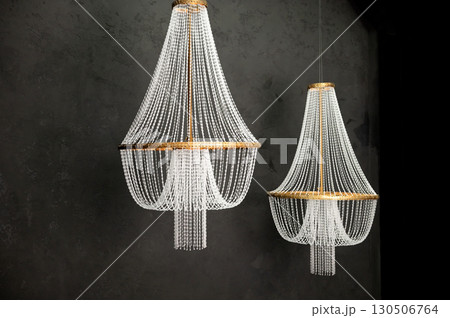 Elegant crystal chandeliers hanging against dark textured background in luxurious setting 130506764