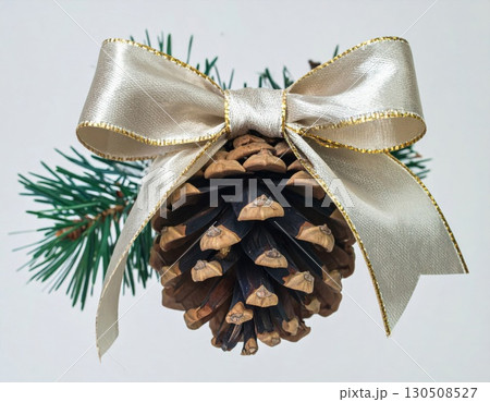 Festive Brown Pinecone Ornament Adorned With Silver Bow and Green Pine Branch on a White Background 130508527