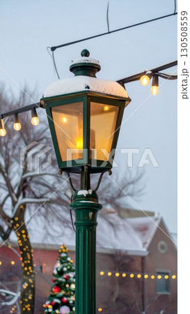 Illuminated Green Street Lamp with Snow and Festive Lights in Winter Town 130508559