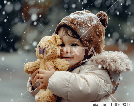 cute little girl hugging a teddy bear while snow falls in a cozy winter outdoor setting 130509018