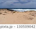 A serene beach scene with sandy dunes, volcanic rocks, and the vast ocean under a cloudy sky, capturing the beauty of La Graciosa. 130509042