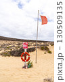 A red flag on a beach indicates dangerous conditions, next to life-saving equipment in a sandy coastal environment. 130509135