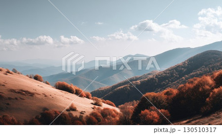 Golden autumn hills cascade down to vibrant orange trees with misty blue mountains rising under the sky 130510317