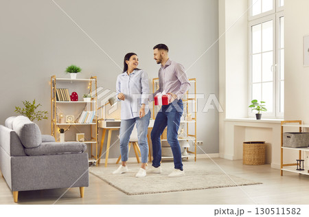Young happy man and woman standing with present gift box in the living room at home. Young happy man and woman standing with present gift box in the living room at home. 130511582