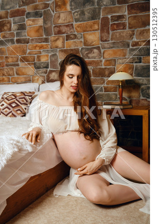 Expectant mother peacefully reflecting in cozy room with rustic brick wall 130512395