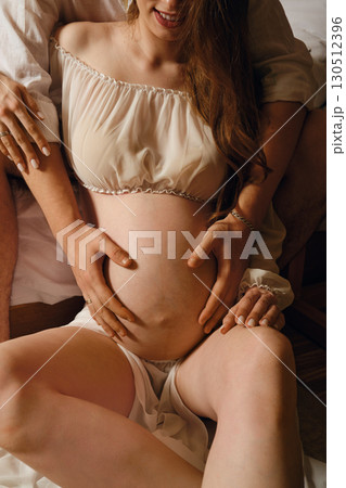 Couple joyfully embracing during pregnancy at home in a cozy bedroom setting 130512396