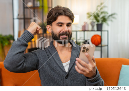 Indian man celebrates mobile game win with smartphone message news smile fist pump joy happy victory Indian man celebrates mobile game win with smartphone message news smile fist pump joy happy victory 130512648