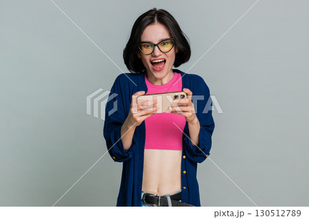 Young woman enthusiastically playing racing drive simulator or shooter video games on smartphone 130512789