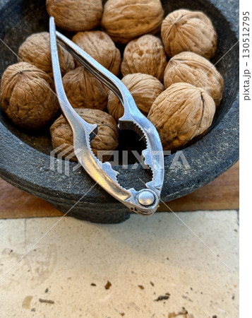Stone bowl filled with whole walnuts and metal nutcracker, rustic kitchen tool in healthy food preparation, closeup plant-based nutrition scene 130512795