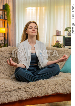 Woman meditating peacefully on home sofa, calm expression, eyes closed, relaxation, taking a break Woman meditating peacefully on home sofa, calm expression, eyes closed, relaxation, taking a break 130512842