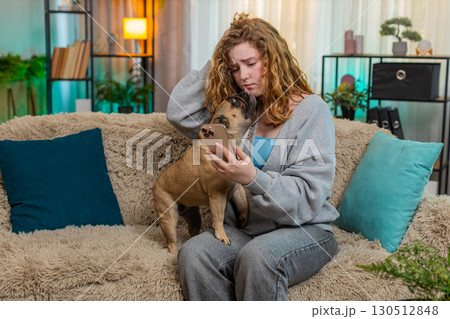 Young woman reacting to bad news on smartphone with pug dog on home sofa, emotional and serious Young woman reacting to bad news on smartphone with pug dog on home sofa, emotional and serious 130512848