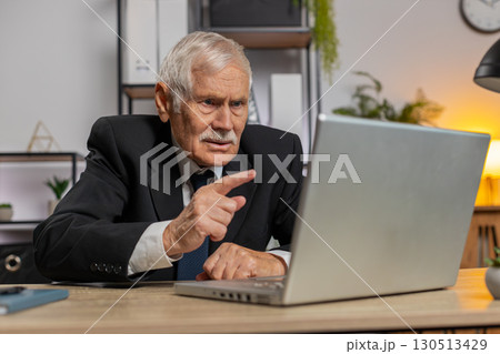 Angry senior freelancer businessman in suit making webcam laptop online video call at home office Angry senior freelancer businessman in suit making webcam laptop online video call at home office 130513429