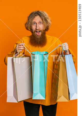 Caucasian man showing shopping bags advertising discounts smiling looking amazed with low prices 130513469
