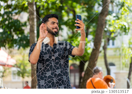 Cheerful man tourist smiling friendly at smartphone camera, waving hands gesturing hello hi greeting Cheerful man tourist smiling friendly at smartphone camera, waving hands gesturing hello hi greeting 130513517
