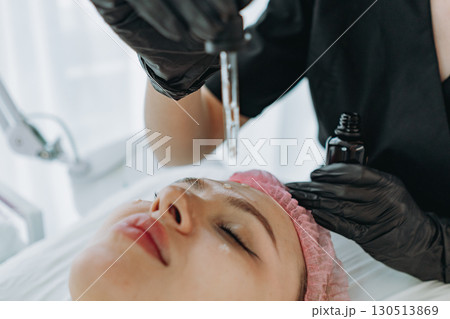 A cosmetologist is dropping serum from a dropper onto a patient's face during a cosmetic procedure 130513869