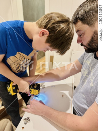 teen age boy helping his father assemble a new piece of furniture with a screwdriver 130513897