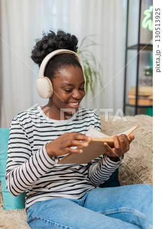African American woman young adult reading novel, deeply focused, sitting on sofa, relaxing at home African American woman young adult reading novel, deeply focused, sitting on sofa, relaxing at home 130513925