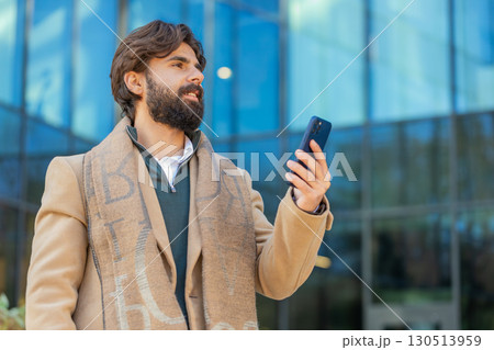 Smiling business man tourist chatting on internet via mobile phone walking on downtown city street 130513959