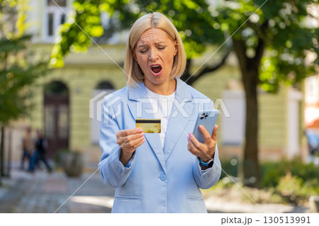 Frustrated mature businesswoman in suit using credit card and mobile phone standing on city street 130513991