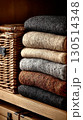 A cozy stack of knitted sweaters next to a wicker basket. 130514348